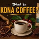 Premium Kona coffee concept image featuring a hot cup of Hawaiian Kona coffee, roasted coffee beans, fresh coffee cherries, and bold typography asking “What Is Kona Coffee?” on a rustic dark background.