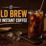 Cold brew with instant coffee featured image showing a glass of cold brew, instant coffee granules, ice cubes, and coffee beans.